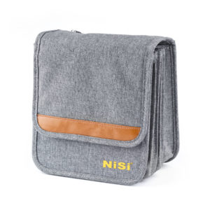 NiSi Caddy 150mm Filter Pouch Pro in grey fabric with a tan leather stripe and yellow NiSi logo, flap closed, three-quarter view showing the pleated spine