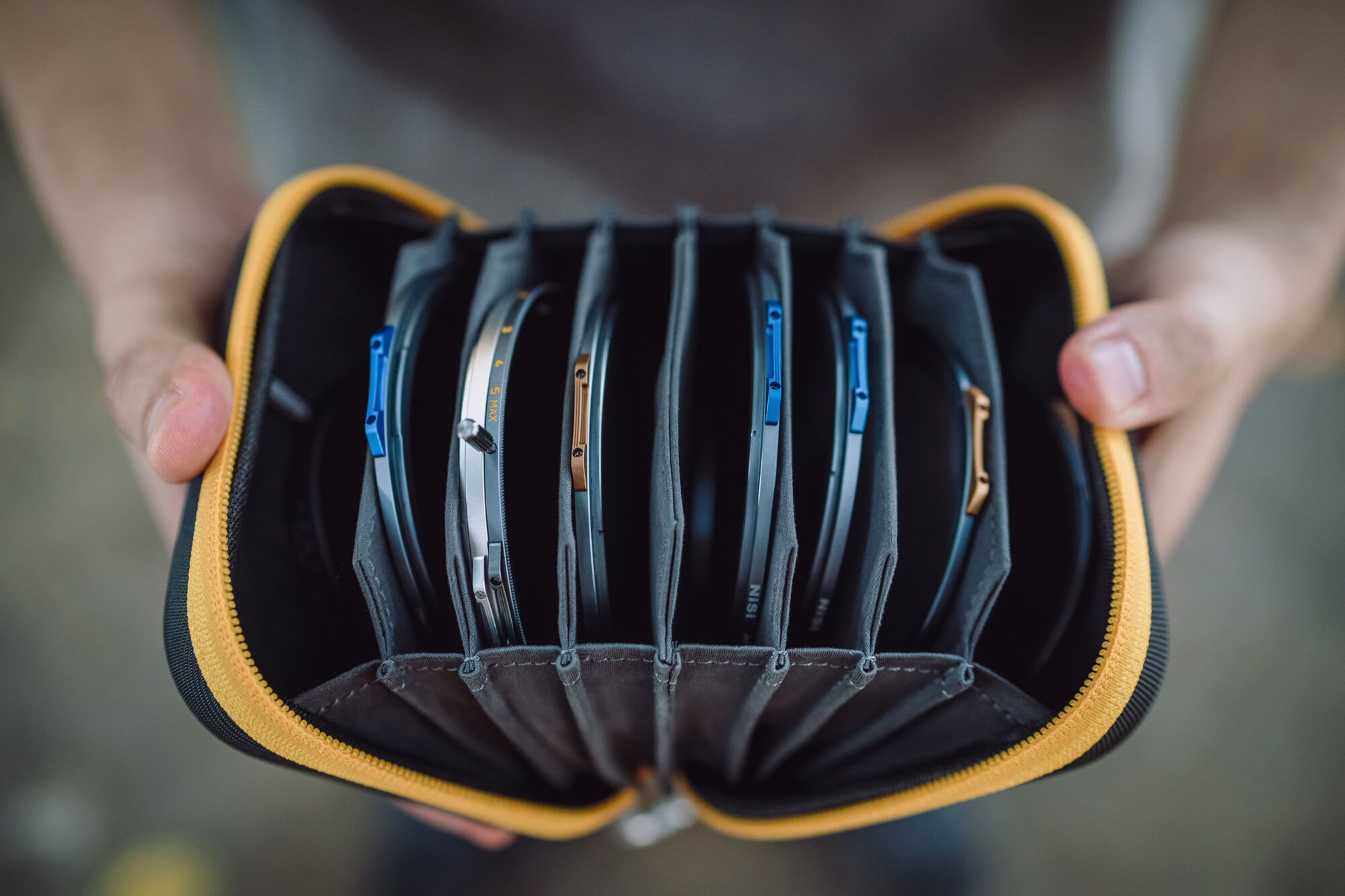 A NiSi Caddy III filter pouch held open in both hands, all eight accordion pockets fanned out with circular filters loaded