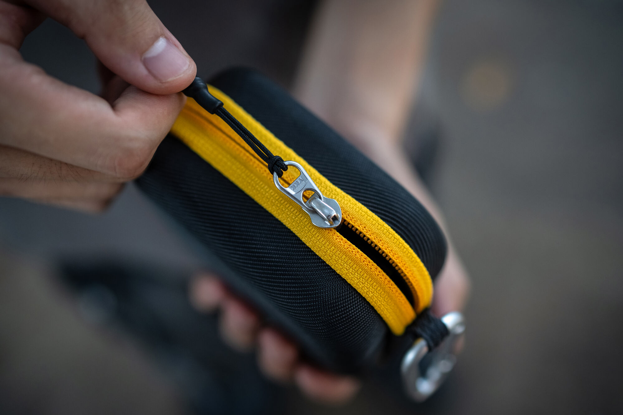A hand pulling the yellow YKK zipper open along the edge of a NiSi Caddy III filter pouch