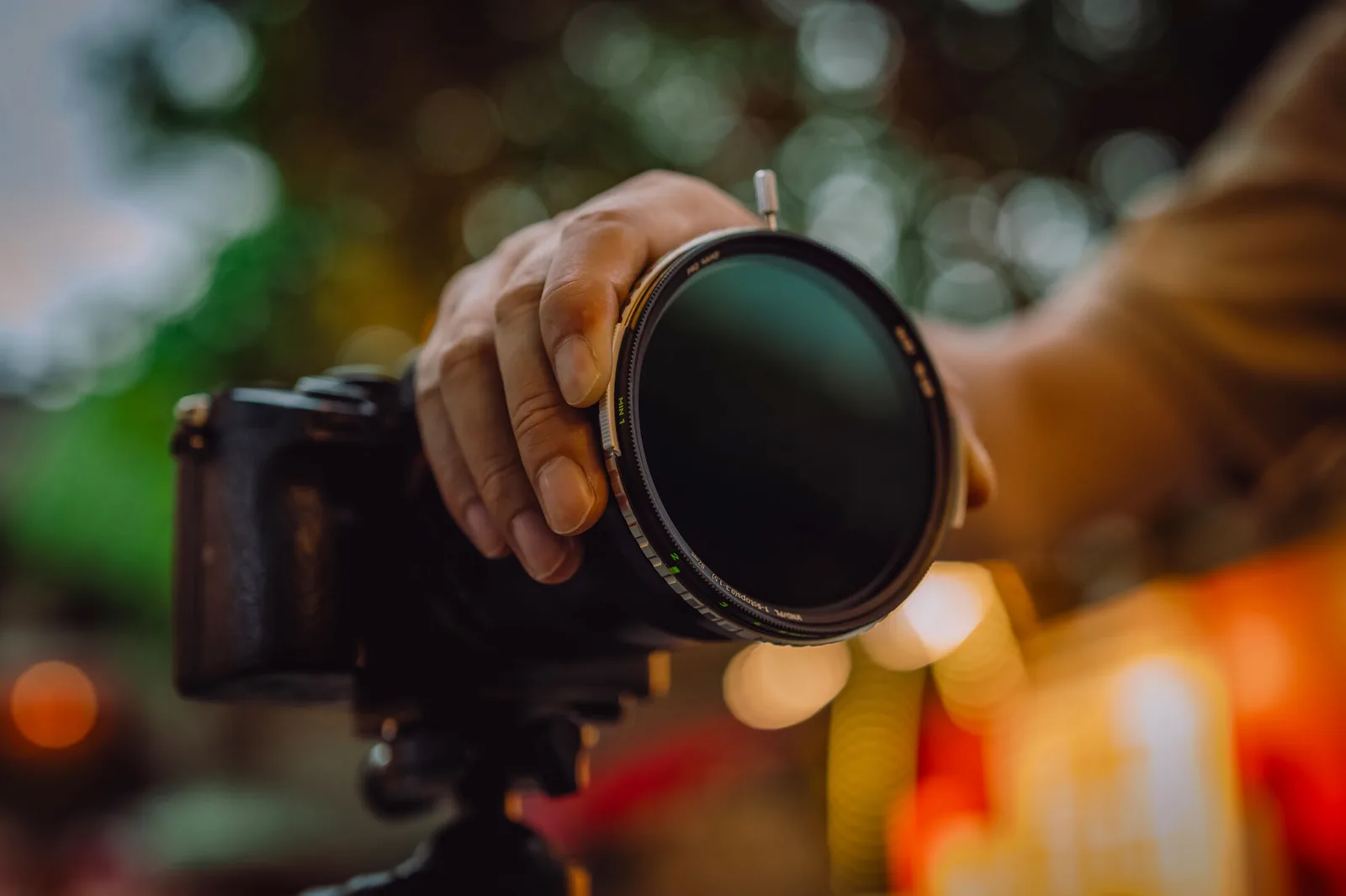 A photographer turning a NiSi True Color VND/PL on a camera on a tripod, with warm bokeh behind