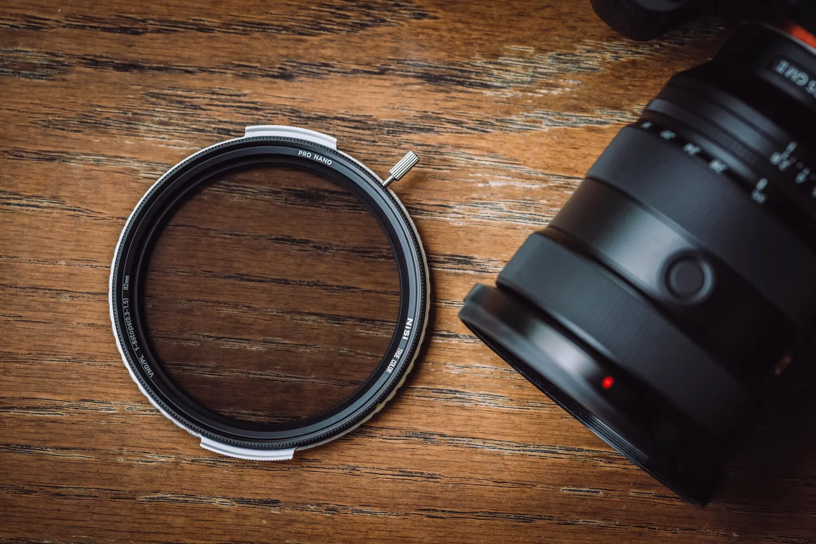 A NiSi True Color VND/PL filter beside a camera lens on a wooden table
