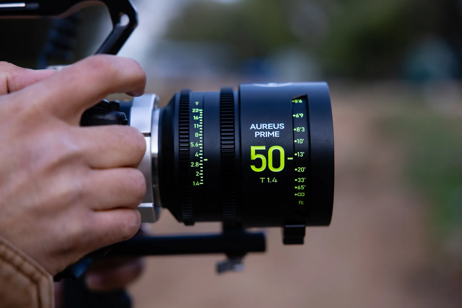 An AUREUS PRIME 50mm lens on a camera, held by hand outdoors
