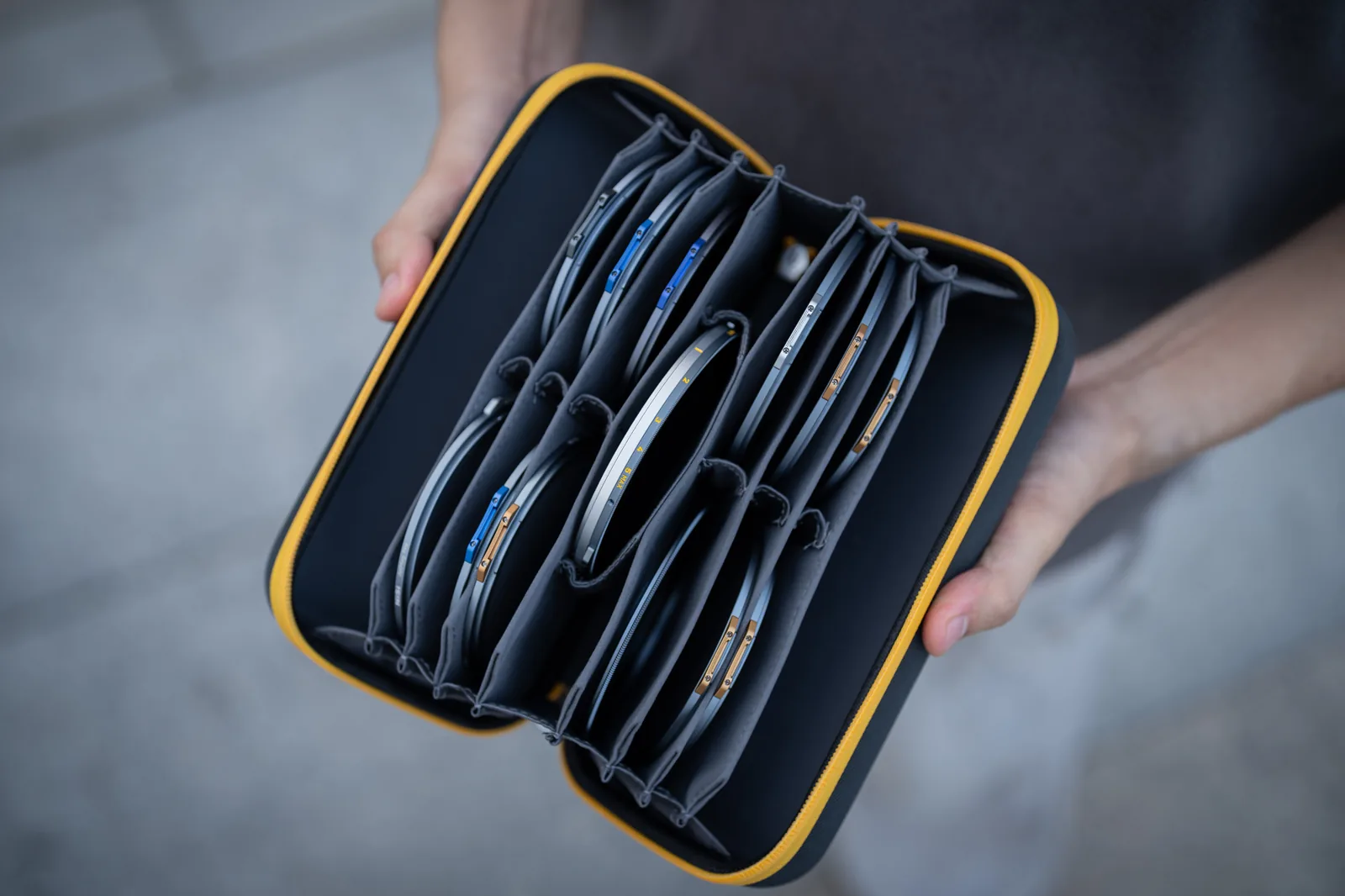 A NiSi Caddy MAX filter pouch held open with both hands outdoors, its long accordion loaded with circular filters