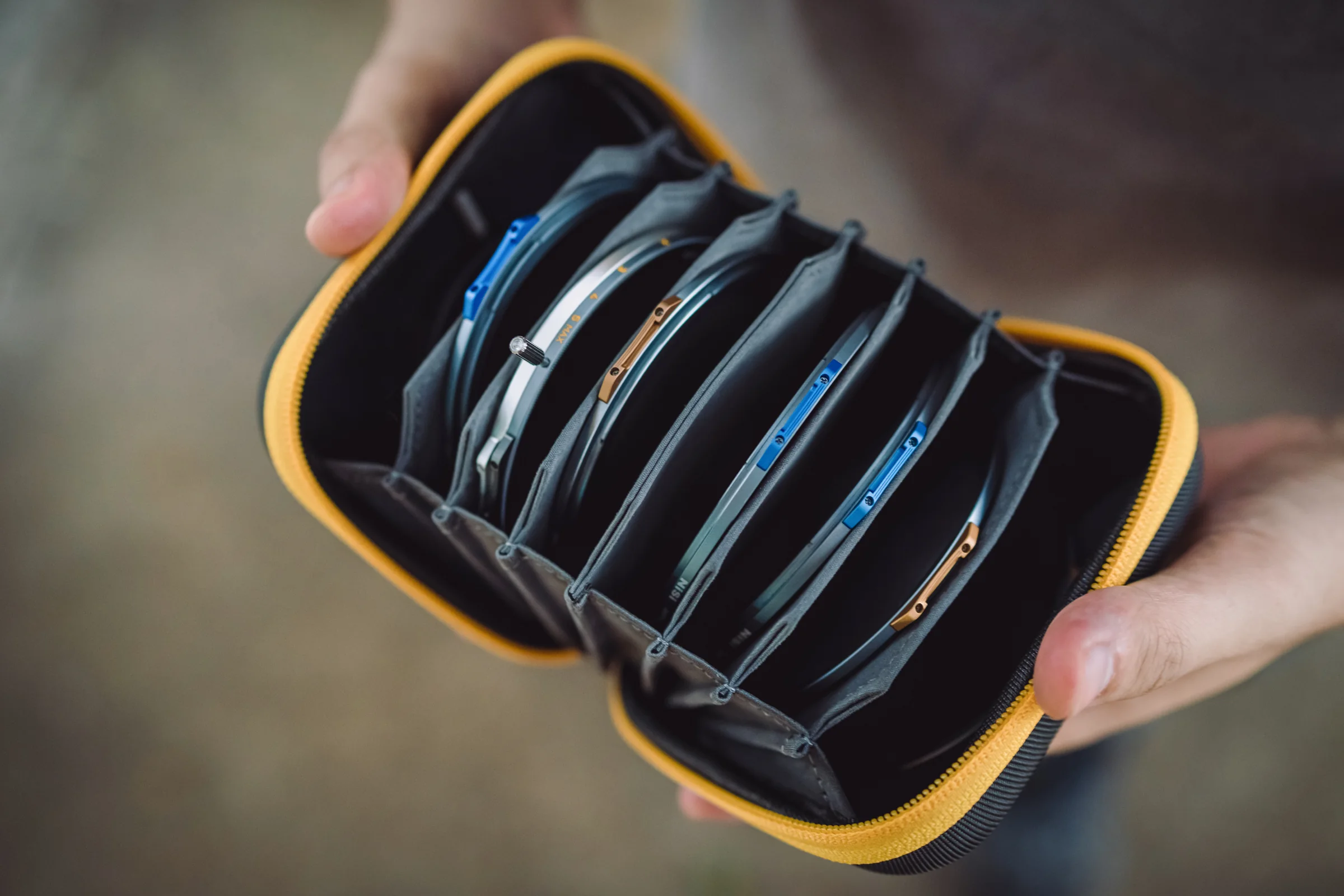 A NiSi Caddy III filter pouch held open in both hands, its accordion pockets fanned out with circular filters in each one