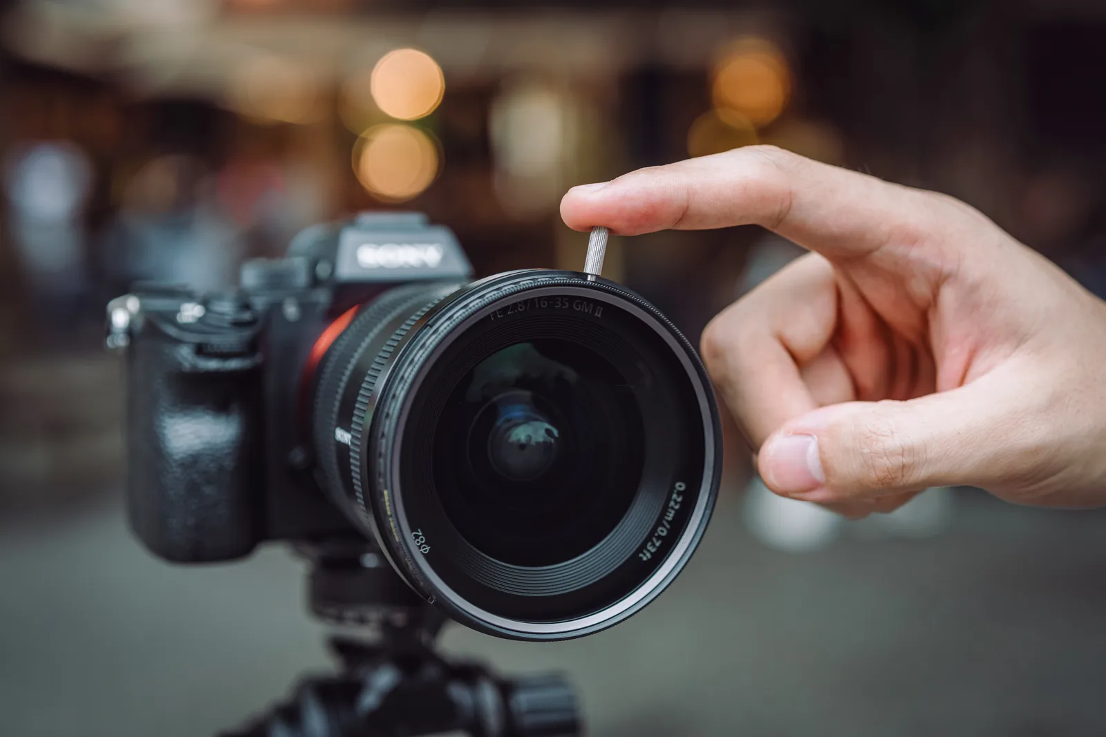 A hand turning the CPL by its knob on a Sony lens
