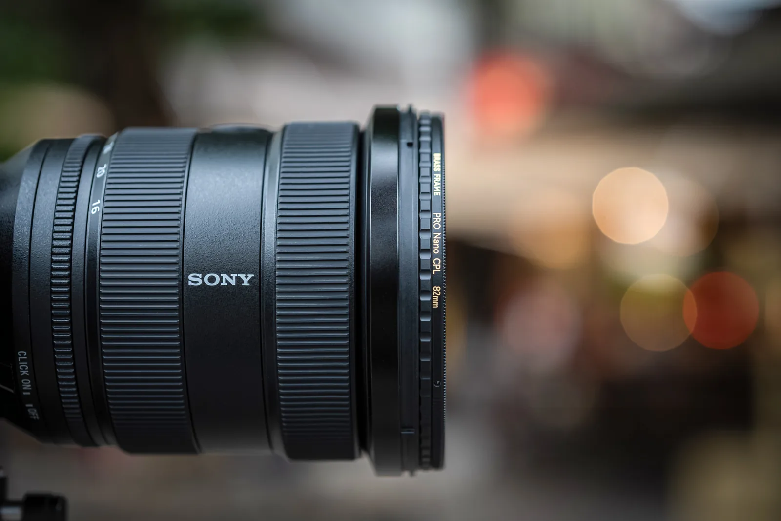 Side view of a Sony lens with the brass frame CPL fitted, against warm bokeh