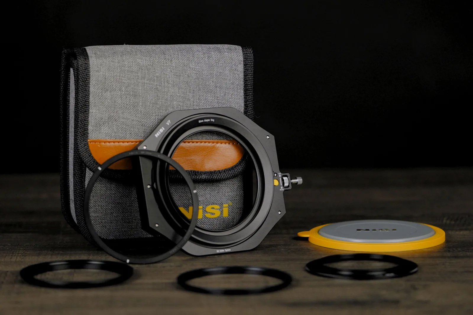 The NiSi V7 100mm filter holder with adapter rings and lens cap in front of its grey storage pouch on a dark wooden surface